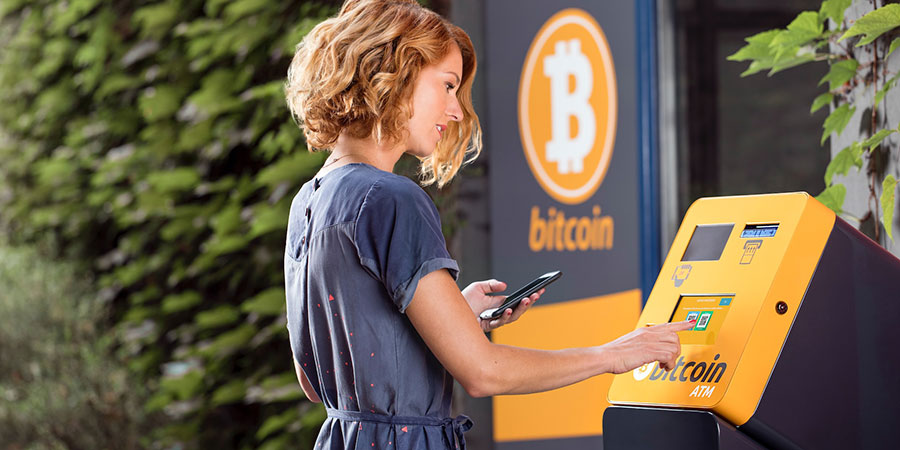 woman with short brown wavy hair holding a mobile phone while using a bitcoin machine